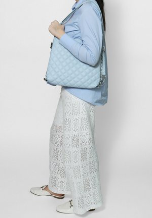 Personne portant un pantalon en crochet blanc, une chemise bleu clair, des chaussures blanches sans lacets, portant un sac à bandoulière matelassé bleu clair avec un détail chaîne.