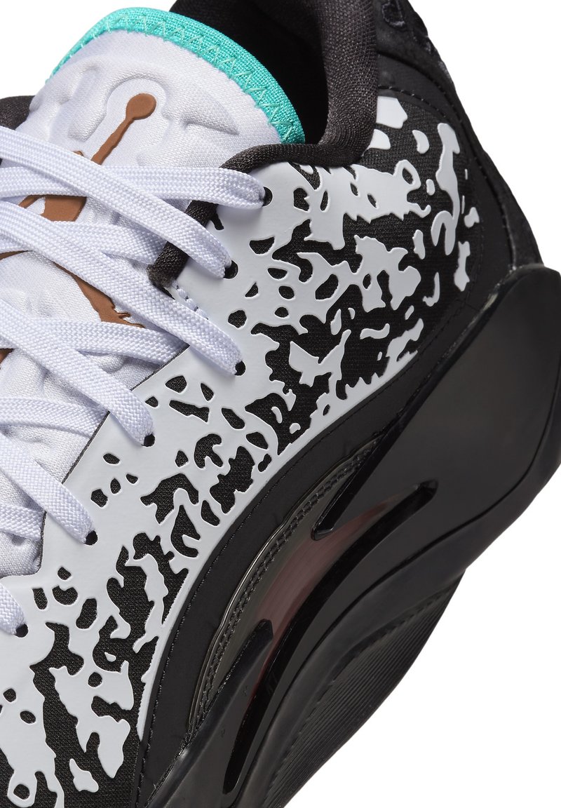 Zapatilla deportiva con una parte superior blanca con un patrón de salpicaduras negras, entresuela negra, acentos turquesas y cordones blancos. Materiales texturizados utilizados.