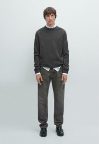 Ciemnoszary sweter z melanżem, z białą koszulą z kołnierzykiem pod spodem, w połączeniu z wyblakłymi szarymi dżinsami i czarnymi butami. Prosty design, luźny krój.