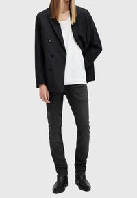 Černý proužkovaný dvouřadý blazer přes bílý tričko, spárovaný s černými džíny a kotníkovými botami, který ukazuje obepnutou siluetu.