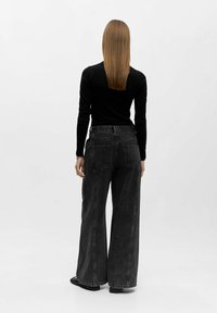 Black wide-leg jeans with contrasting stitching, high waist, and back pockets. Paired with a fitted black long-sleeve top.