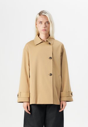 Beige, oversized coat with a button-up front, large collar, and cuffed sleeves. Made from smooth fabric, featuring two side pockets.