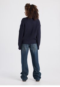 Navy ribbed sweater with a relaxed fit, paired with light blue baggy jeans. The texture of the sweater is chunky and thick.