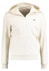 Sudadera con cremallera en color beige claro, hecha de una tela suave, que cuenta con un bolsillo tipo canguro, puños de canalé y un pequeño logo verde de Lacoste en el pecho.