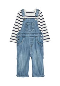 Pantalones de mezclilla en azul claro con tirantes ajustables, herrajes plateados y un bolsillo en el pecho, combinados con una camiseta de rayas azul marino y blanca de manga larga.