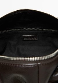 Borsa aperta in pelle nera che mostra l'interno in tessuto nero vuoto con una tasca interna con cerniera chiusa e denti della cerniera in metallo visibili.