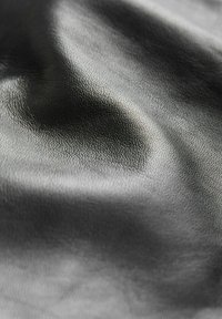 Černá texturovaná kůže s hladkým povrchem, vykazující jemný lesk a záhyby. Zaměření na složité vzory zrna po celé ploše materiálu.
