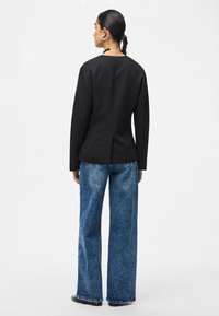 Černý přizpůsobený sako s dlouhými rukávy, spárované s volnými modrými džíny. Sako má detail na zadním švu a čistý výstřih.