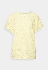 Haut en dentelle jaune pâle, doté d'un col rond et de manches courtes. Motif floral avec des détails ajourés sur toute la surface.
