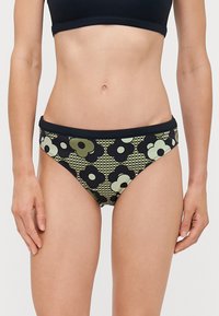 Fekete és zöld mintás bikini alsó virágmintával, rugalmas derékpánttal és mérsékelt takarással. Geometrikus háttér és sima textúra.