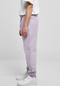 Lavender Jogginghose mit lockerem Schnitt, elastischem Bund, seitlichen Taschen und gerippten Bündchen, kombiniert mit weißen Sneakers.