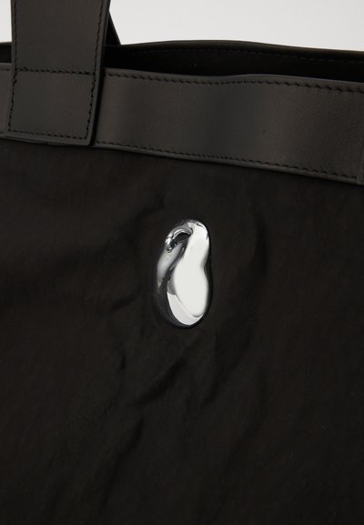 Must mustra kott, millel on sileda nahast ülemine käepide ja läikiv, ümmargune kroomdetail. Tekstuuriga pind, millel on peened voldid.