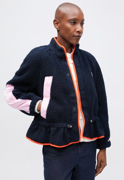 Mornarska fleece jakna s roza detajli in peplum robom. Ima visok ovratnik, gumbe in stranske žepke. Svetlo oranžni detajli poudarjajo dizajn.