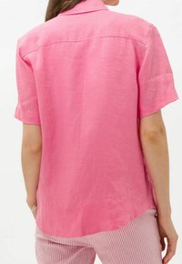 Donna che indossa una maglietta rosa a maniche corte e pantaloni a righe rosa e bianchi, mostrata di spalle su uno sfondo neutro.