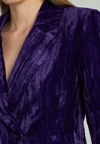Blazer viola in velluto con una finitura testurizzata, dotato di rever a punta e chiusura con un bottone singolo. Vestibilità su misura e spalle strutturate.