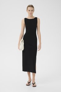 Black, sleeveless maxi dress with a slightly curved neckline and side slit. Paired with a light-colored clutch and flip-flops.