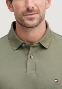 Polo verde oliva in tessuto strutturato, con abbottonatura a due bottoni e un piccolo logo ricamato sul petto.