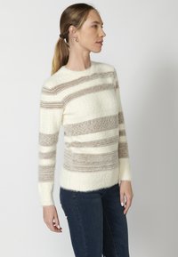 Kreemja ja beežikuidulise triibuga kampsun pehmest, karvast materjalist. Ümmargune kaelus, pikad varrukad, ribakujundusega aksendid varrukate otstes ja alläärs.