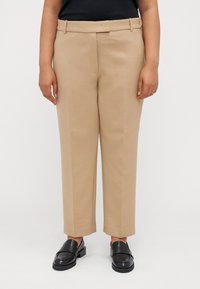 Kaki bukser laget av glatt stoff, med rett snitt, beltehemper og sidelommer, kombinert med svarte loafers.