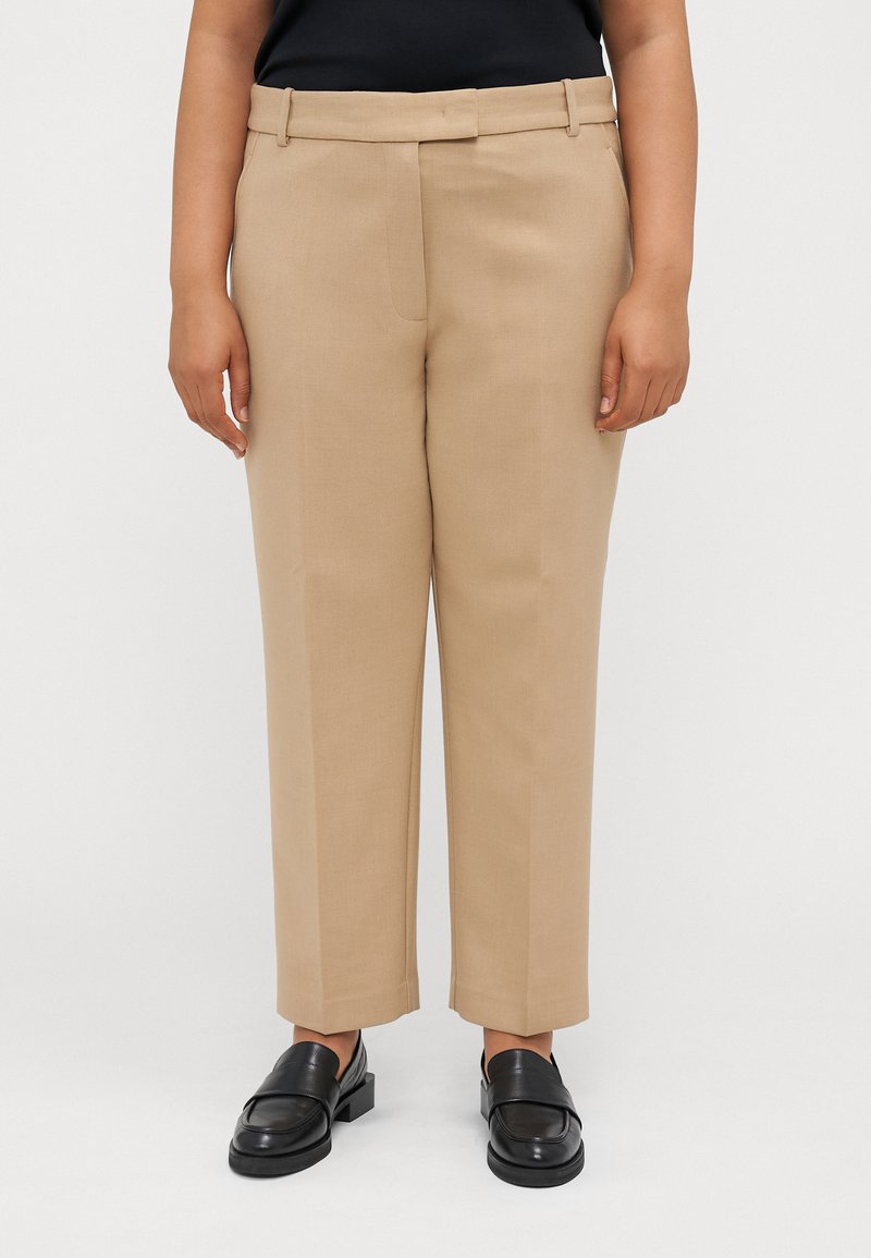 Kaki bukser laget av glatt stoff, med rett snitt, beltehemper og sidelommer, kombinert med svarte loafers.