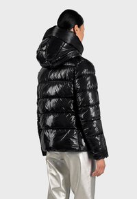 Giacca piumino nera con un esterno lucido e trapuntato, cappuccio e design aderente, abbinata a pantaloni argentati lucidi.