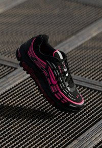 Melnas sneakers ar rozā un sudraba akcentiem. Īpaši iezīmēti ar teksturētu augšdaļu, redzamu gaisa amortizāciju un šņorēšanas dizainu ar izteiktu logotipu.