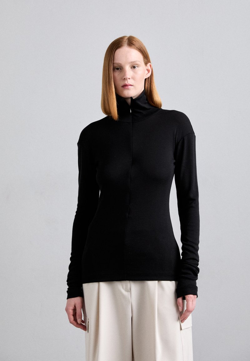 Mustapaita, jossa on pitkät hihat, korkea kaulus ja vetoketju, valmistettu sileästä neuloksesta, istuva malli ja pitkät hihansuut. Yhdistetty vaaleisiin housuihin.