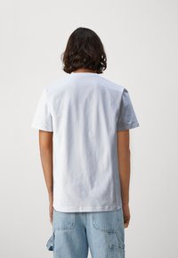 Tricou alb cu mâneci scurte, din bumbac neted, cu decolteu rotund și croi lejer. Fără modele sau grafică vizibilă pe spate.