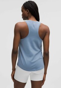 Jasnoniebieski bezrękawnik z okrągłym dołem i wycięciem na plecach, w połączeniu z białymi szortami sportowymi. Gładka tekstura materiału.