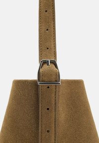 Ceinture en suede marron avec une boucle en métal argenté, dotée de trous réglables, soulignant une surface texturée et un design épuré.