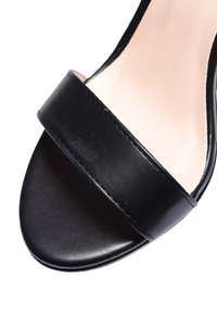 Sandalo nero con tacco alto in pelle liscia, dotato di una larga fascia superiore. Design con punta aperta, finitura lucida e cuciture minime.