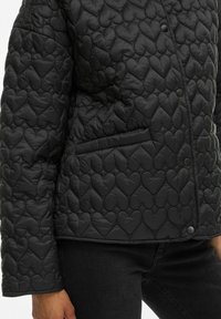 Juodas siuvinėtas švarkas su širdelės raštu, su užsegimu mygtuku ir šonine kišene. Pagamintas iš minkštos, tekstūruotos medžiagos.