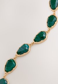 Green gemstone necklace featuring irregularly shaped stones set in gold-toned metal links, creating a textured, layered appearance.