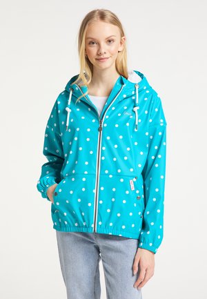 Veste de pluie turquoise à pois blancs, avec des poignets élastiques et des poches avant. Comprend une fermeture éclair et une capuche avec cordon de serrage.