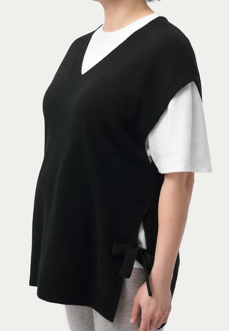 Svart stickad väst med v-ringning, korta ärmar och sidofästen. Bärs över en vit T-shirt med avslappnad passform och ribbad nederkant.