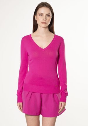 Maglione fucsia a maniche lunghe con scollo a V. Realizzato in tessuto morbido con polsini e orlo a coste. Abbinato a pantaloni corti plissettati coordinati.