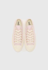 Light pink canvas sneakers feature a rounded toe, cream rubber sole, gold eyelets, and flat cream laces. No visible branding on the exterior.