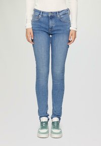 Kapeakan denim skinny berwarna biru muda, dengan pinggang sedang, lima saku, dan jahitan halus. Dipadukan dengan sneakers hijau dan putih.