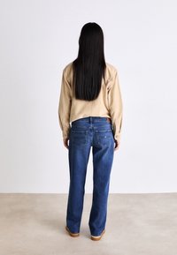 Beige long-sleeve shirt tucked into blue wide-leg jeans with back pockets, minimal stitching, and a smooth texture. Brown shoes complement the outfit.