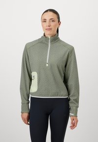 Janes leve em tom verde claro, com fecho de zíper de um quarto, apresentando um padrão texturizado, com um bolso frontal em uma tonalidade mais clara e acabamento contrastante branco ao longo da barra.