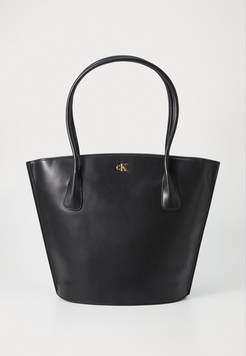 Sac cabas en cuir noir avec deux anses et petit logo doré "cK" centré près du haut.