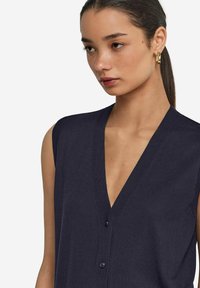 Ärmlös marinblå stickad topp med djup V-ringning, knappframsida och ribbad detaljer. Slät textur, lättviktig tyg.