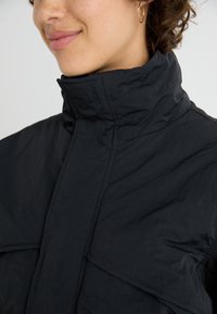 Schwarze Puffjacke mit hohem Kragen, strukturiertem Stoff und sichtbaren Nähdetails, die ein modernes Design bietet.