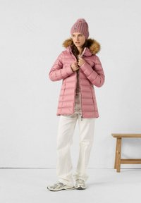 Gewatteerde, lichtroze jas met een capuchon van nep-bont, heeft een ritssluiting en elastische manchetten. Gekleed met crèmekleurige broek en zilveren sneakers.