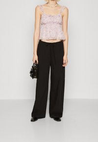 Blommönstrad, genomskinlig rosa topp med volangband, kombinerad med lösa svarta byxor och en liten svart handväska. Platta svarta skor kompletterar outfiten.