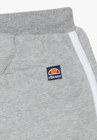 Grå joggebukser med ribbestrikket liv, med en liten "Ellesse" logo og lyseblå side-striper. Myk bomullstekstur.