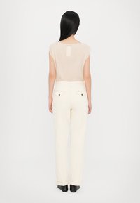 Beige sheer top with short sleeves and back opening, paired with cream-colored straight-leg pants. Black footwear completes the outfit.
