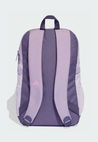 Fioletowy plecak z siatkowanymi bocznymi kieszeniami, wyściełanymi paskami i uchwytem na górze. Wykonany jest z teksturowanej tkaniny z subtelnym różowym logo.