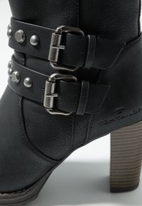 Bottine en cuir noir avec deux larges brides, ornée de boucles en métal et de clous. Finition texturée remarquable et talon empilé. Logo de la marque affiché.