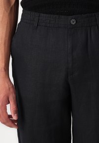 Czarne lniane spodnie z elastycznym paskiem w talii i jednym guzikiem. Gładka tekstura z delikatnym połyskiem, z bocznymi kieszeniami i schludnymi szwami.